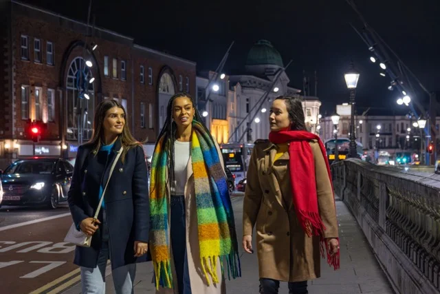Three adults walking beside a bridge in Cork city at night